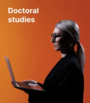 Doctoral studies in Kaunas. A young KTU PhD student with glasses, holding a laptop and working on it, against a vibrant orange background.
